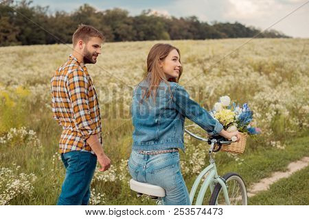 Side View Of Young Lovers With Retro Bicycle In Field With Wild Flowers