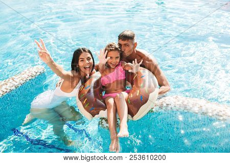 Joyful young family having fun together at the swimming pool outdoors in summer, swimming with inflatable ring donut
