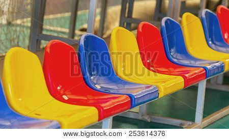 Multicolored Empty Plastic Chairs In The Stands Of The Stadium. Many Empty Seats For Spectators In T