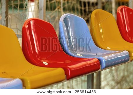 Multicolored Empty Plastic Chairs In The Stands Of The Stadium. Many Empty Seats For Spectators In T
