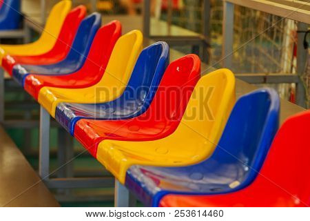 Multicolored Empty Plastic Chairs In The Stands Of The Stadium. Many Empty Seats For Spectators In T