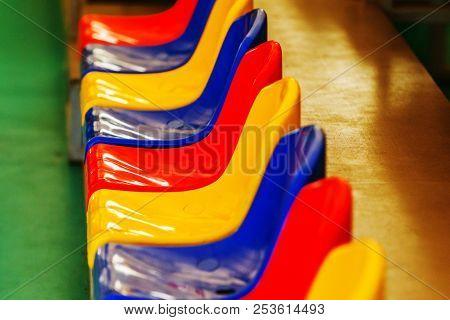Multicolored Empty Plastic Chairs In The Stands Of The Stadium. Many Empty Seats For Spectators In T