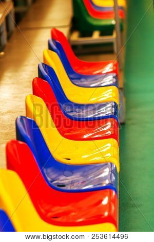 Multicolored Empty Plastic Chairs In The Stands Of The Stadium. Many Empty Seats For Spectators In T