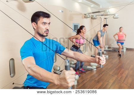Portrait of a determined fit young man exercising with the resistance bands of an anchor gym system mounted on wall in a trendy fitness club