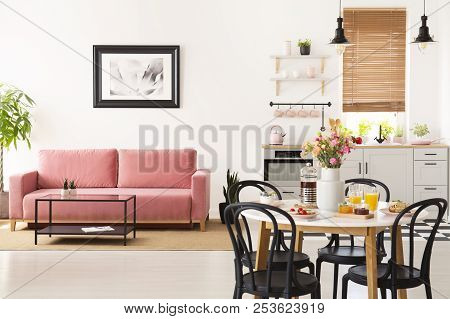 Dining Table With Breakfast And Fresh Flowers Standing In Bright Apartment Interior With Pink Sofa,