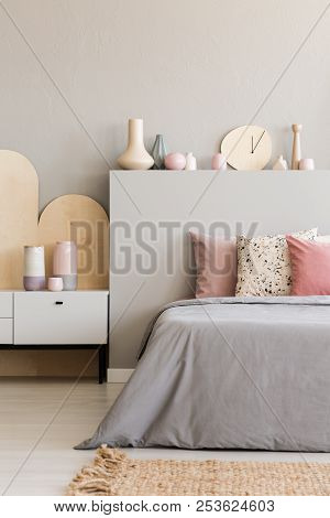 Pink Pillows On Grey Bed With Headboard In Bedroom Interior With Rug And Cabinet. Real Photo