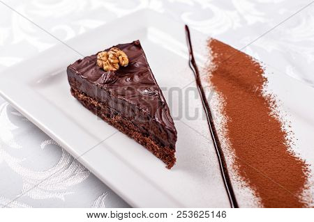 Piece Of Sacher Chocolate Cake, Cocoa Biscuit With Walnut Filling And Dark Chocolate Icing Served On