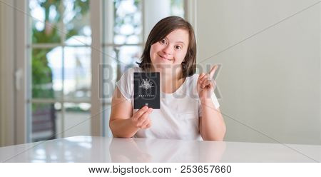 Down syndrome woman at home holding australian passport surprised with an idea or question pointing finger with happy face, number one