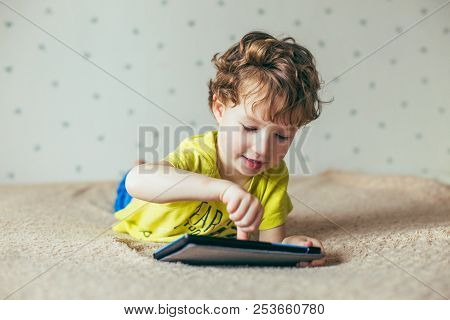 Little Cute Boy In A Green T-shirt Playing Games On A Tablet And Watching Cartoons. Addiction Concep