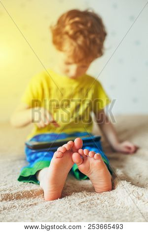 Little Cute Boy In A Green T-shirt Playing Games On A Tablet And Watching Cartoons. Addiction Concep