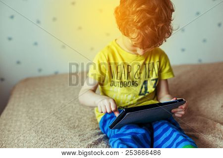 Little Cute Boy In A Green T-shirt Playing Games On A Tablet And Watching Cartoons. Addiction Concep