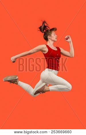 Freedom In Moving. Mid-air Shot Of Pretty Happy Young Woman Jumping And Gesturing Against Orange Stu