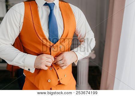 Elegant Male Groom Buttons Up Orange Waistcoat, Dressed In Festive Clothes, Prepares For Wedding Cer
