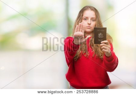 Young blonde woman holding passport of United States of America with open hand doing stop sign with serious and confident expression, defense gesture
