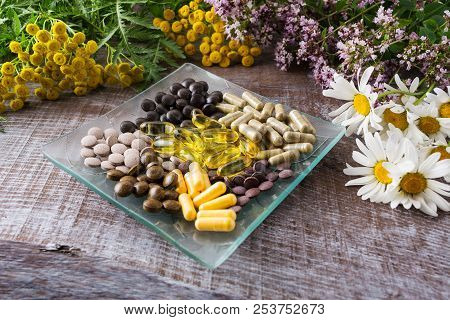 Ayurvedic Herbal Pills On The Glass Plate And Wild Chamomile, Tansy, Oregano. Healthy Life Concept