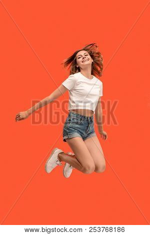 Freedom In Moving. Mid-air Shot Of Pretty Happy Young Woman Jumping And Gesturing Against Orange Stu