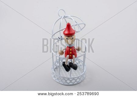 Metal Cage And Little Puppet Pinocchio Made Of Wood