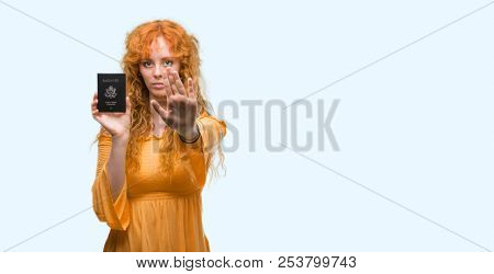 Young redhead woman holding passport of United States of America with open hand doing stop sign with serious and confident expression, defense gesture