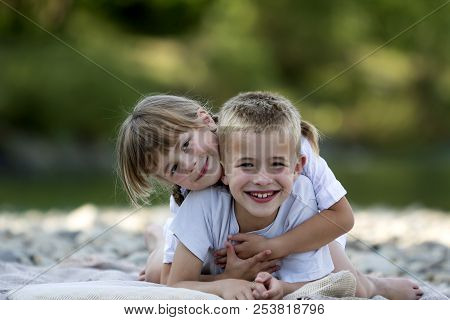 Two Young Happy Cute Blond Smiling Children, Boy And Girl, Brother And Sister Laying Embraced On Peb