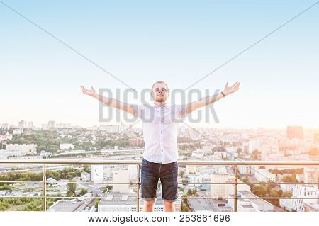 Man's Portrait On A High Rise Building Balcony Overlooking City With Hands Rised Up To Sky, Feeling 