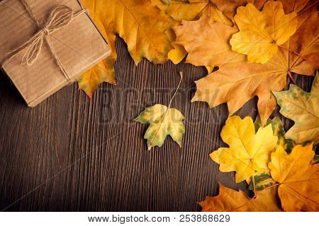 cardboard box tied with string on a bow on a wooden background in autumn leaves, holiday gift on Thanksgiving Hellouin. view from the top. copy space