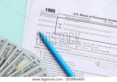1065 Tax Form Lies Near Hundred Dollar Bills And Blue Pen On A Light Blue Background. Us Return For 