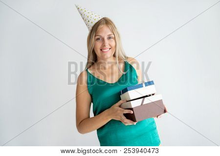 Portrait Of Happy Blonde Birthday Girl Holding Gifts. Content Young Caucasian Woman In Birthday Cap 