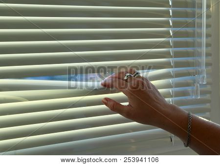 The Woman's Hand Bends The Rail Of The Horizontal Blinds To Look Out The Window.
