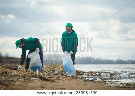 Active men in green uniform working on shore and collecting garbage for envirnomental conservation