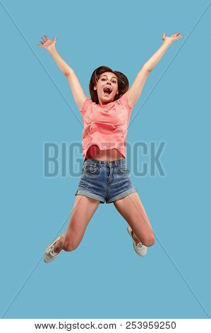 Freedom In Moving. Mid-air Shot Of Pretty Happy Young Woman Jumping And Gesturing Against Blue Studi