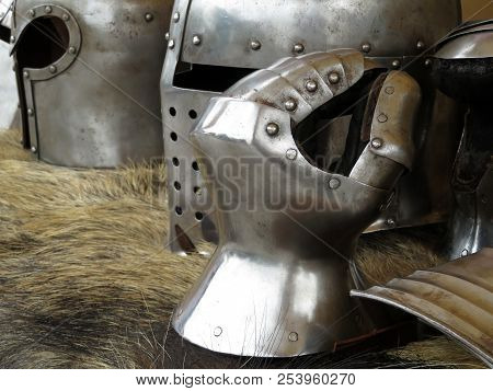 Medieval Helmets And Gloves On A Bearskin Rug. Armor Of Middle Ages, Knightly Equipment, Armory Forg