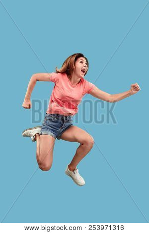 Freedom In Moving. Mid-air Shot Of Pretty Happy Young Woman Jumping And Gesturing Against Blue Studi