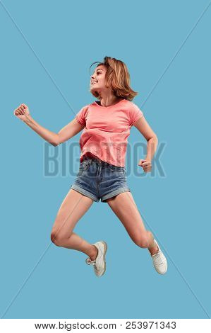 Freedom In Moving. Mid-air Shot Of Pretty Happy Young Woman Jumping And Gesturing Against Blue Studi