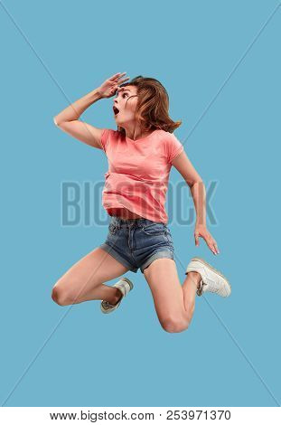 Freedom In Moving. Mid-air Shot Of Pretty Happy Surprised Young Woman Jumping Against Blue Studio Ba