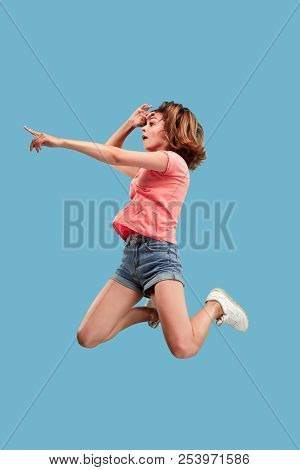 Freedom In Moving. Mid-air Shot Of Pretty Happy Young Woman Jumping And Pointing By Finger Against B