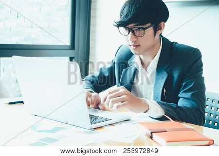Handsome Young Businessman Sitting In A Modern Corporate Environment, And Working With Laptop Comput