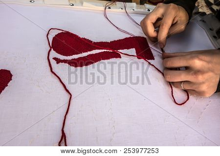 Hands Of An Embroiderer With A Needle And Red Threads Over A White Canvas Close-up