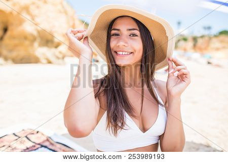 Young Beauty Latin Woman In Bikini And Straw Hat Sitting Under Sun Umbrella On The Beach Near Sea Co