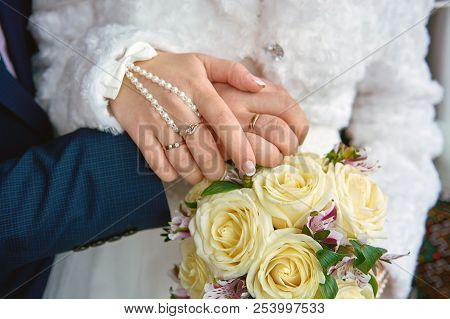 Hands Newlyweds With A Bouquet. A Newly Weding Couple Place Their Hands On A Wedding Bouquet