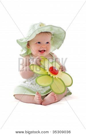 Adorable Baby Girl In Pretty Dress And Sun Hat Sits And Plays With Big Toy Flower