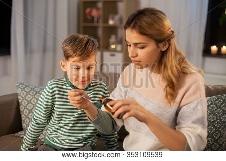 family, health and people concept - sad mother pouring antipyretic medication or cough syrup to spoon for ill little son at home