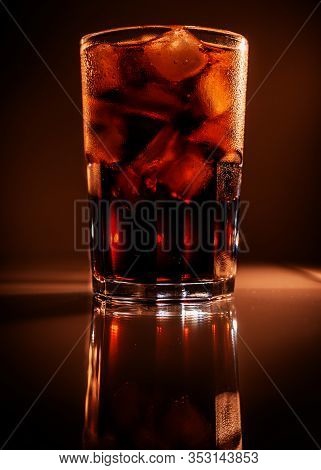 Glass Of Cola With Ice On Brown Background With Reflection. Close-up Of Cold Refreshing Carbonated D