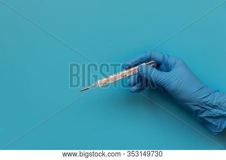 Hand Of Medic Wearing Blue Latex Glove Holding Termometer Which Shows High Temperature On Blue Backg