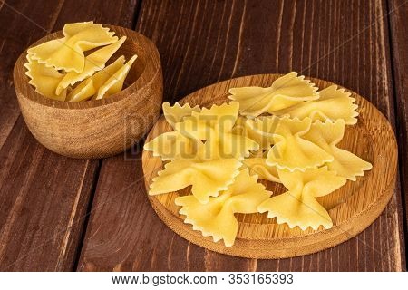 Lot Of Whole Yellow Pasta Farfalle In Bamboo Bowl On Round Bamboo Coaster On Brown Wood