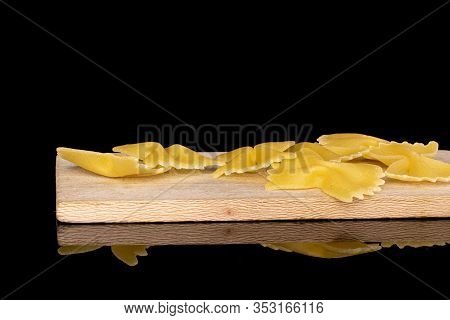 Lot Of Whole Yellow Pasta Farfalle On Wooden Cutting Board Isolated On Black Glass