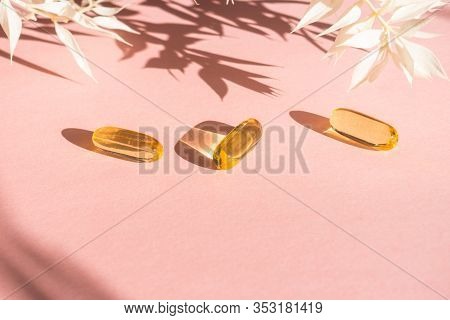 Oil Yellow Gelatin Capsules On Pink Background With Flower Shadow, Vitamins And Antioxidant Concept 