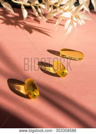 Oil Yellow Gelatin Capsules On Pink Background With Flower Shadow, Vitamins And Antioxidant Concept 
