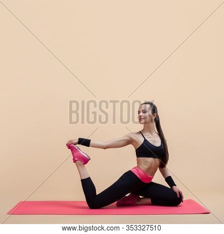 A Young Attractive Girl With A Ponytail, A Brunette, Sits In A Mermaid Pose On A Pink Yoga Mat, On A