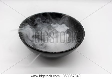Clean Smoke And Vapor In Motion Over Black Bowl Of Dry Ice In Water Isolated On White Background.