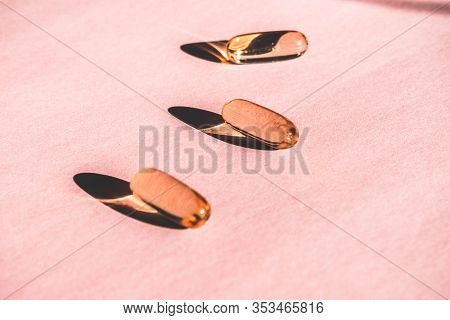 Oil Yellow Gelatin Capsules On Pink Background With Flower Shadow, Vitamins And Antioxidant Concept 
